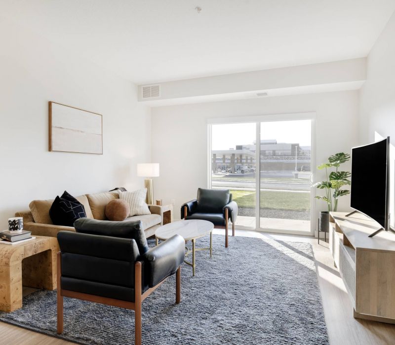 Modern living room with a sofa, two chairs, TV, coffee table, and large window letting in natural light.