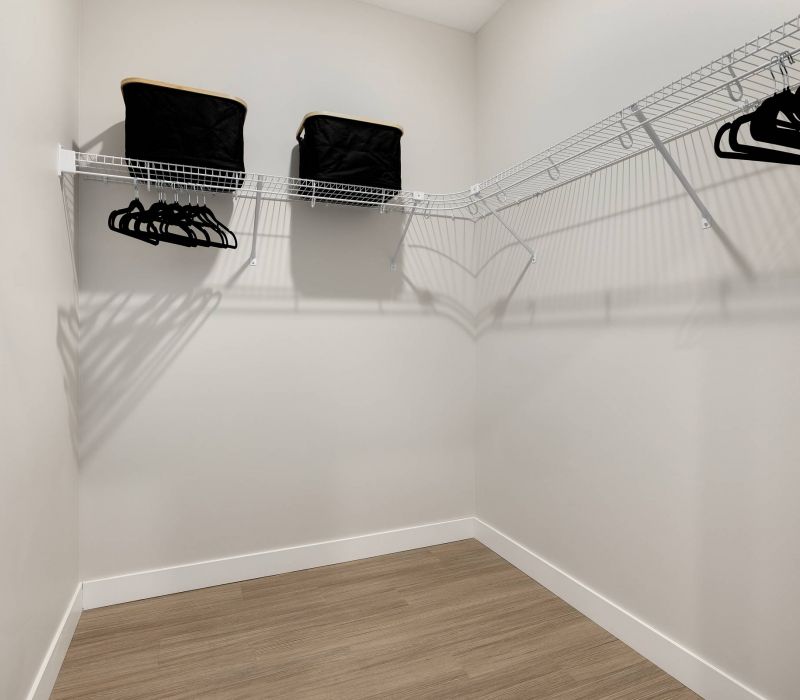 Empty walk-in closet with wire shelves, black storage bins, and black hangers on a light wood floor.