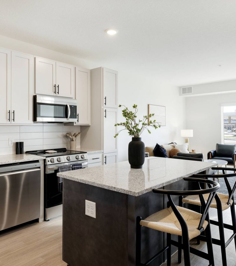Modern kitchen with white cabinets, stainless steel appliances, and a dining island with two chairs.