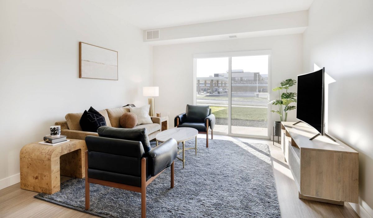 Modern living room with a sofa, two chairs, TV, coffee table, and large window letting in natural light.