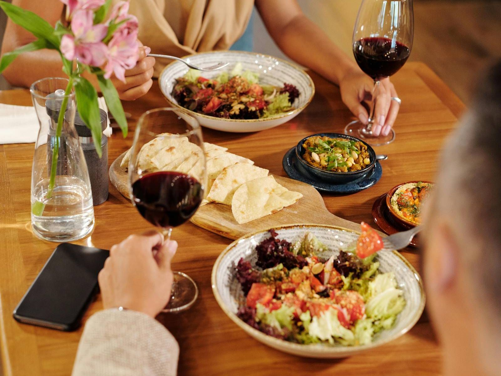 Two people dining at a restaurant, enjoying salads and wine, with flowers and food on the table.