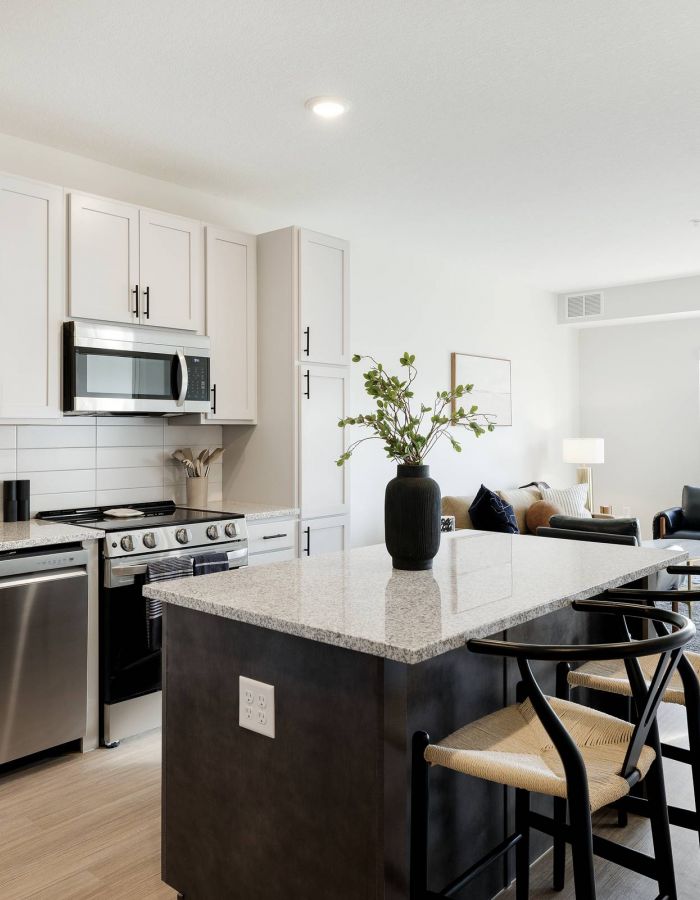 Modern kitchen with white cabinets, stainless steel appliances, island seating, and a bright living area.