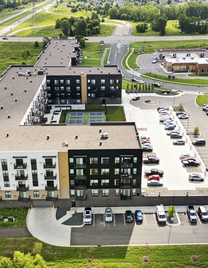 Aerial view of a modern apartment complex with a parking lot, surrounded by roads and greenery.