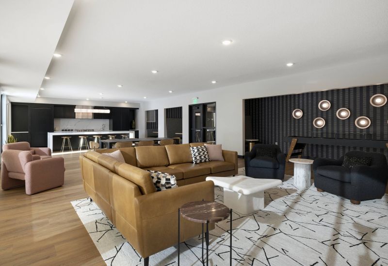 Modern open-concept lounge with brown sofa, armchairs, patterned rug, and kitchen in the background.