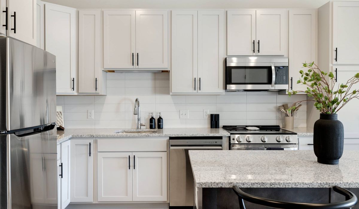 Modern kitchen with white cabinets, stainless steel appliances, and a vase with green branches on the island.
