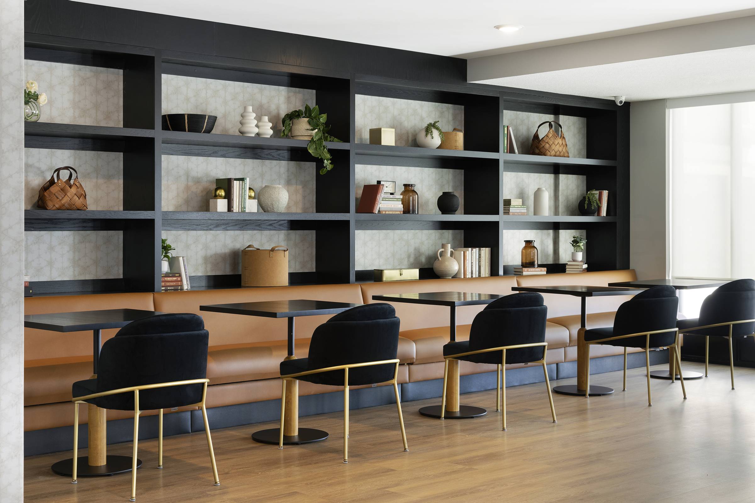 Modern cafe with black chairs, tan benches, black tables, and shelves with books and decorative items.