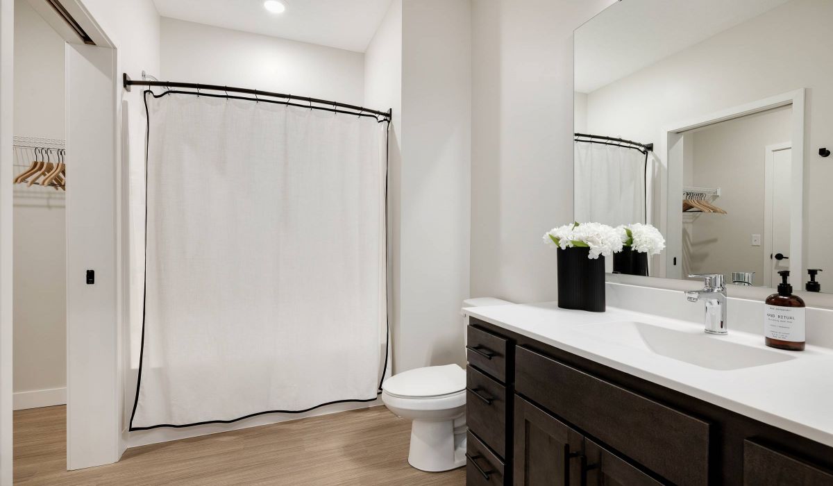 Modern bathroom with a white shower curtain, dark vanity, white countertop, and a vase of white flowers.