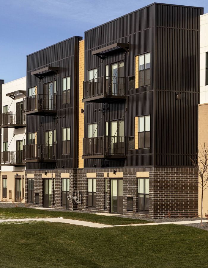 Modern apartment building with balconies, large windows, and a grass lawn in front under a clear sky.