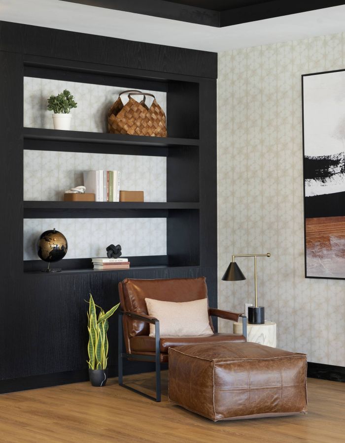 Modern living room with black shelves, leather chair and ottoman, potted plant, and abstract wall art.